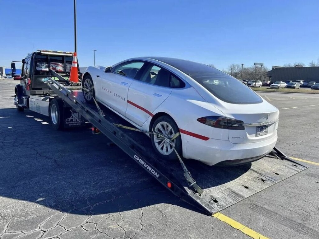 Tesla electric vehicle being loaded onto flatbed tow truck for long distance towing