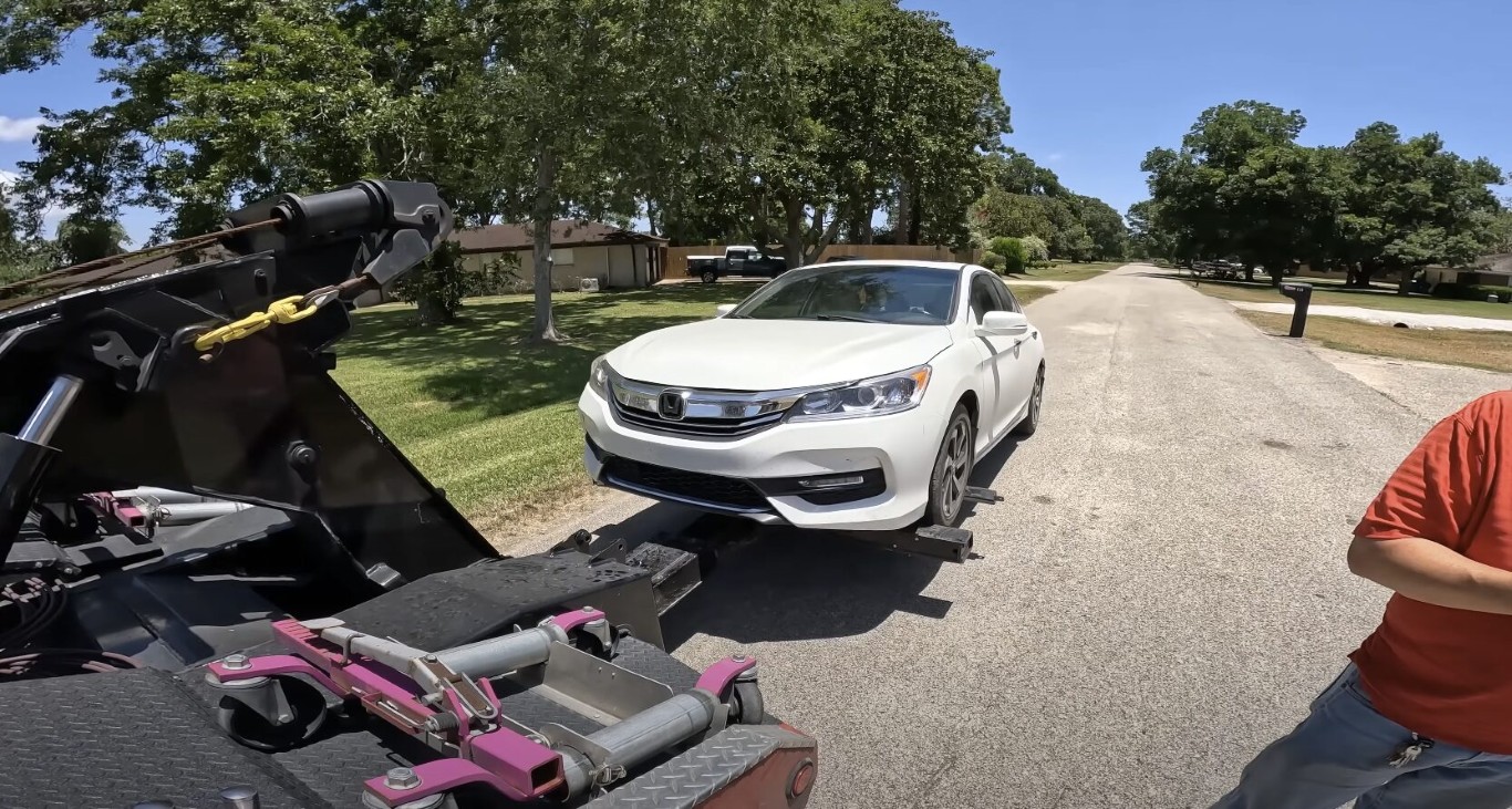 Professional tow truck operator loading white Honda onto wheel-lift in Lindenhurst, NY